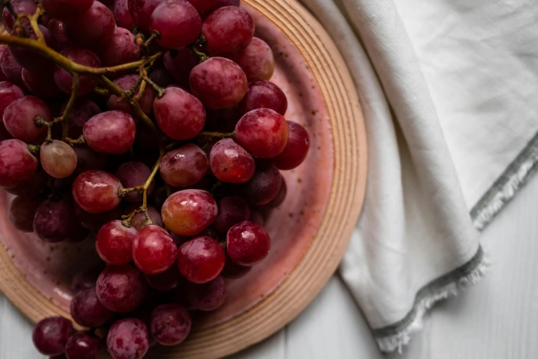 a close up of a plate of grapes on a table, by Helen Stevenson, trending on unsplash, visual art, maroon red, linen, natural soft light, high quality product image”