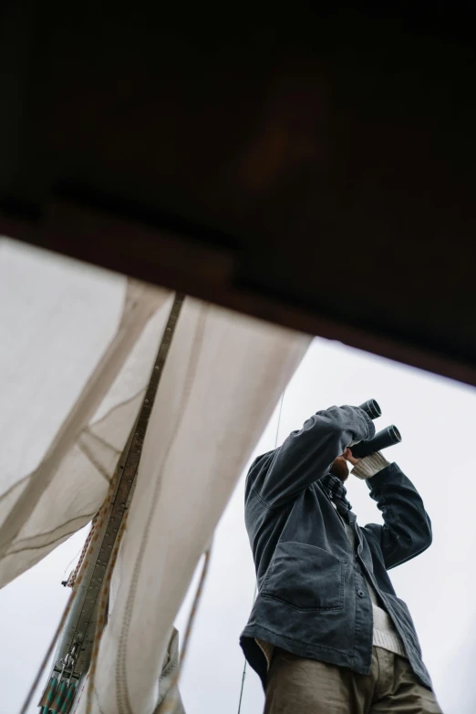 a man standing on top of a boat talking on a cell phone, unsplash, visual art, binoculars, grey, hiding, sails