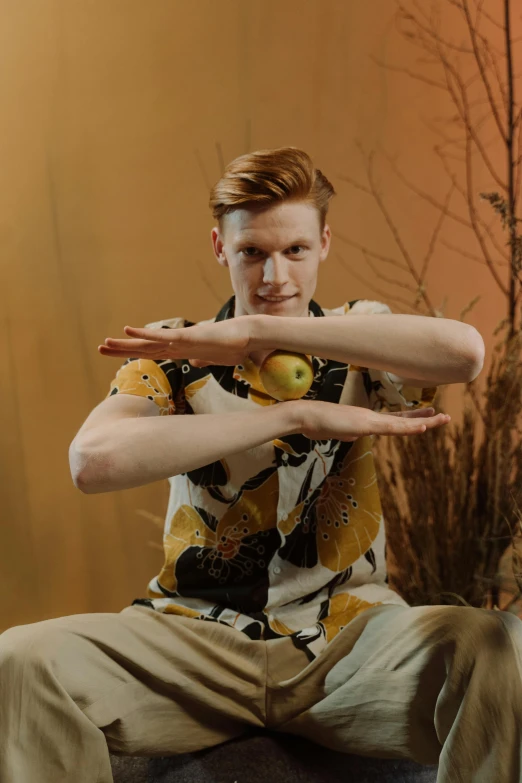 a man sitting on a chair holding an apple, by Lee Gatch, unsplash, renaissance, wearing yellow floral blouse, ginger hair, posing with crossed arms, dynamic dancing pose