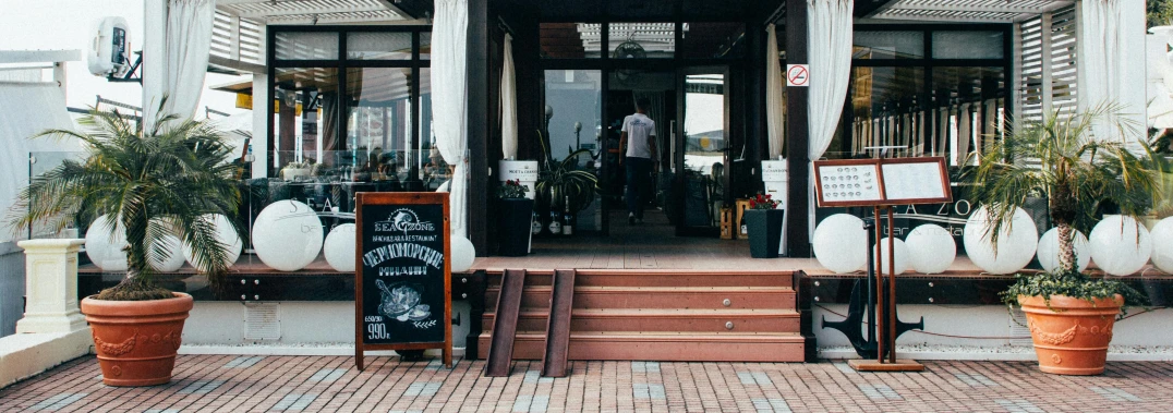 a building with a bunch of potted plants in front of it, trending on unsplash, aussie baristas, exiting store, boardwalk, about to enter doorframe