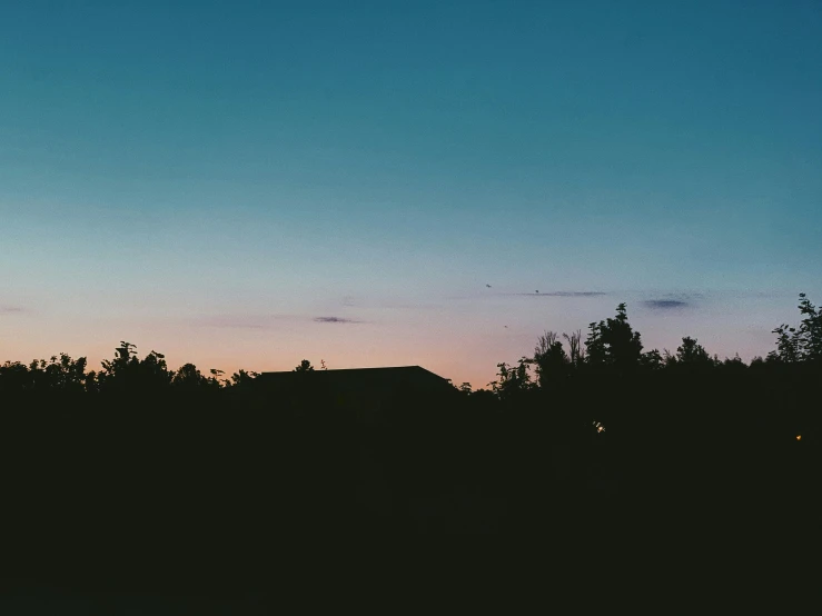 a silhouette of a house in the distance with trees in the foreground, inspired by Elsa Bleda, unsplash contest winner, summer evening, fades to the horizon, cloudless sky, dark and muted colors