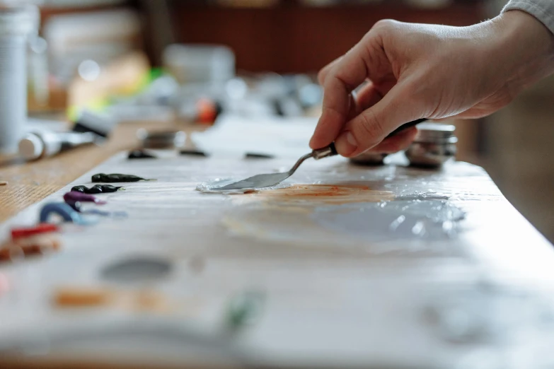 a person cutting a piece of paper with a knife, a photorealistic painting, inspired by Kyffin Williams, trending on pexels, silver palette, resin painting, hand on table, oil on canvas