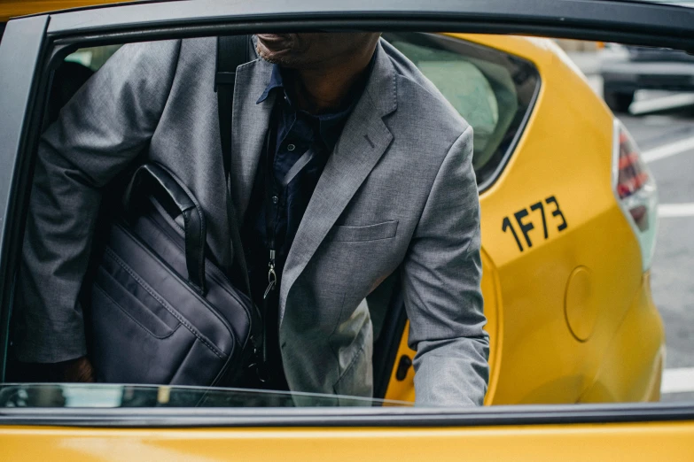 a man in a suit getting out of a taxi, a photo, yellow and charcoal leather, carrying a saddle bag, in gunmetal grey, thumbnail