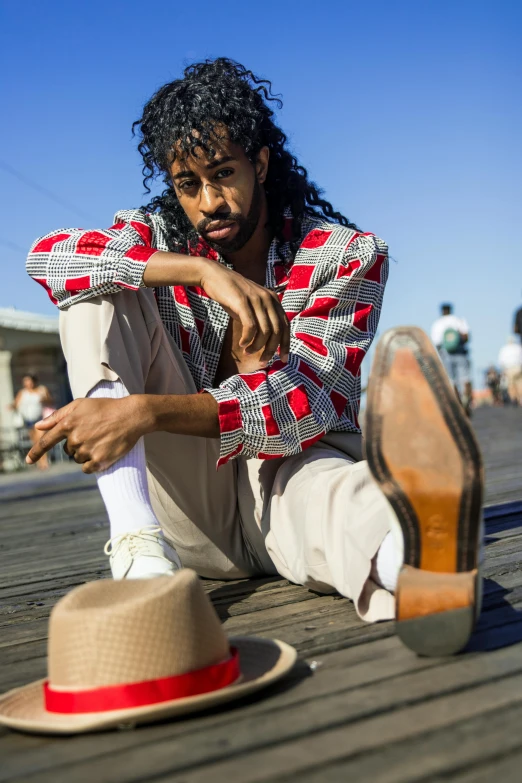 a man sitting on top of a wooden floor next to a hat, by Washington Allston, trending on unsplash, renaissance, imaan hammam, wearing a colorful men's suit, red shoes, los angeles 2 0 1 5