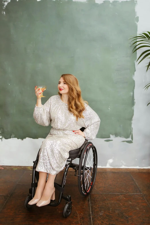 a woman sitting in a wheelchair in front of a chalkboard, inspired by Hannah Tompkins, unsplash, renaissance, drinking champagne, wearing silver silk robe, on a pale background, wearing a cocktail dress