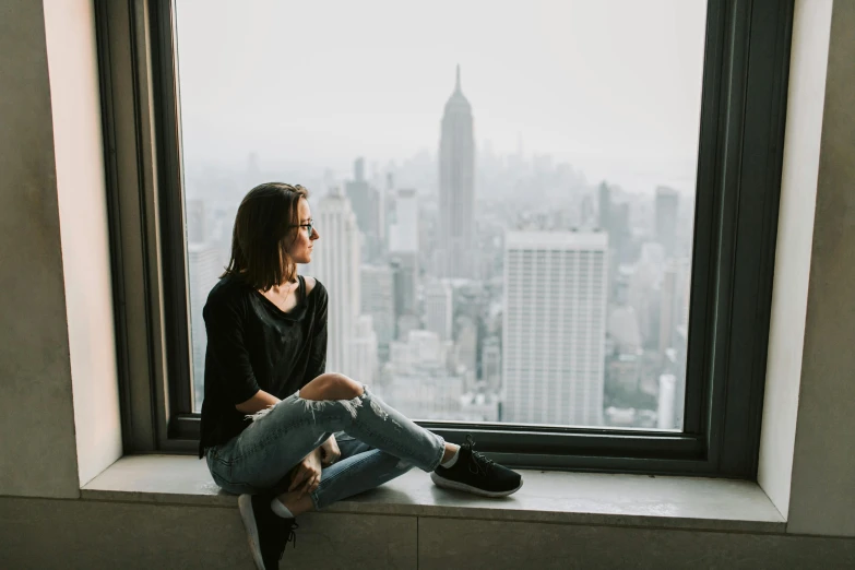 a woman sitting on a window sill looking out at a city, a picture, trending on unsplash, wearing a dark shirt and jeans, watching new york, teenage girl, sitting in a waiting room