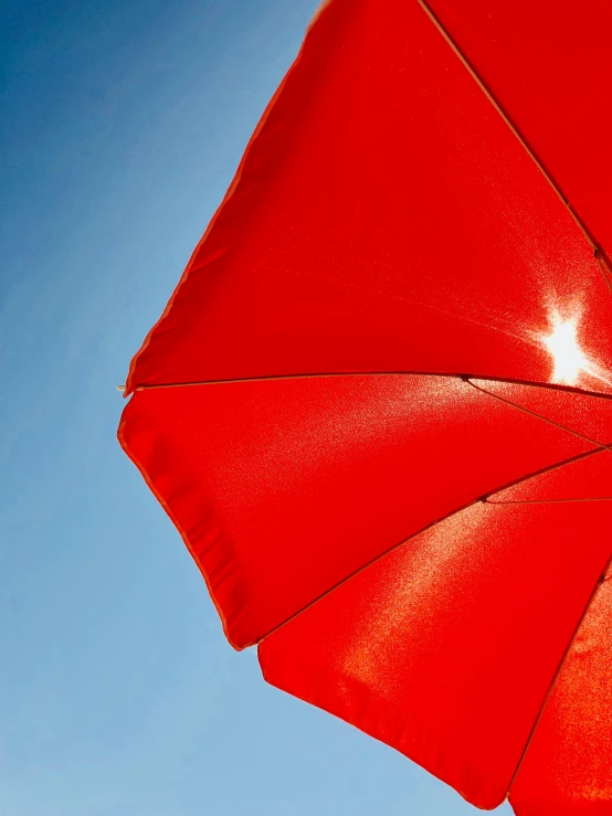 a red umbrella sitting on top of a sandy beach, in the sun, profile image