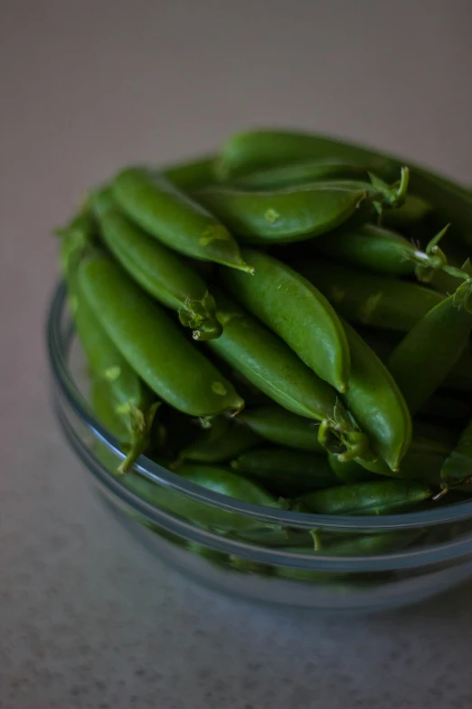 a bowl filled with green peas on top of a table, by Ben Zoeller, salvia, piled around, with slight stubble, vanilla