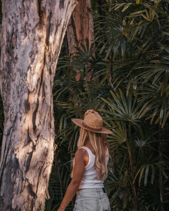 a woman in a hat standing next to a tree, by Maggie Hamilton, unsplash contest winner, slightly tanned, lush exotic vegetation, sydney hanson, profile image