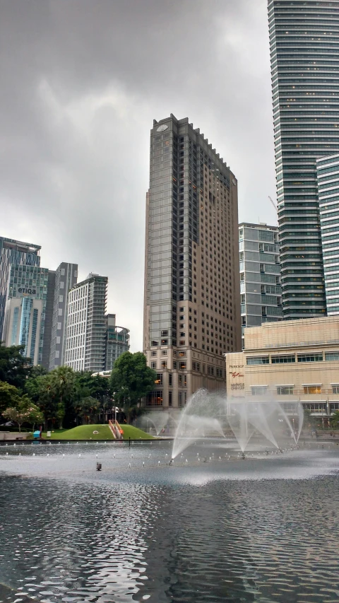 a fountain in the middle of a city with tall buildings in the background, jakarta, building facing