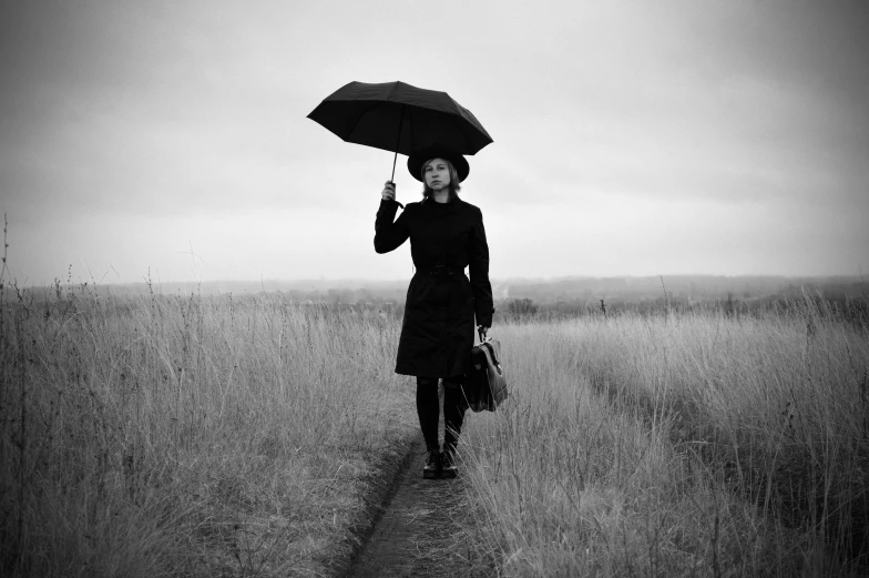 a black and white photo of a woman holding an umbrella, a black and white photo, pexels, conceptual art, ffffound, dressed in black, journey, in a field