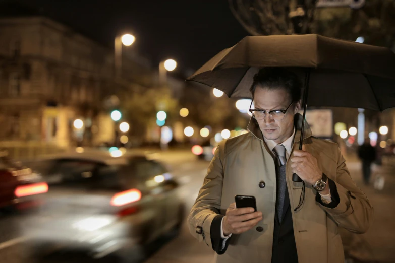 a man holding an umbrella while looking at his cell phone, street lighting, avatar image, high-resolution, thumbnail