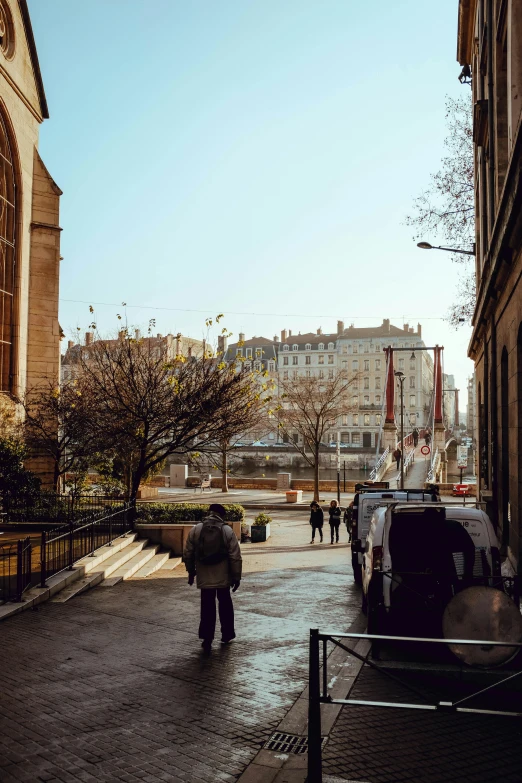 a man walking down a street next to tall buildings, a photo, pexels contest winner, paris school, sunny morning light, with a french garden, khreschatyk, early spring
