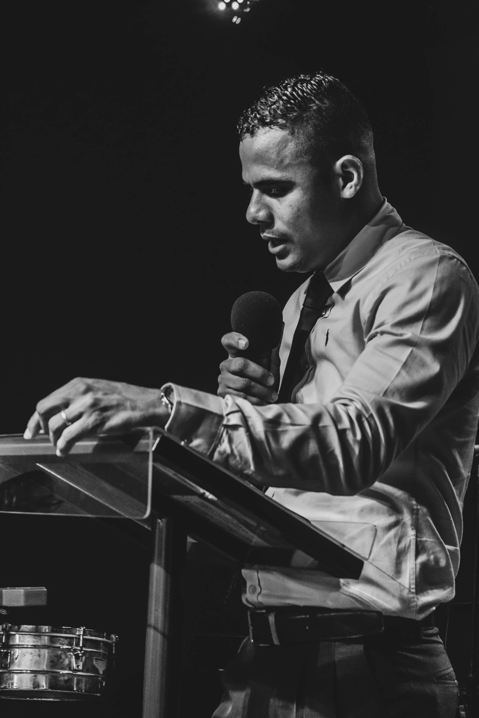 a man standing at a podium with a microphone, a black and white photo, unsplash, christian saint, thiago alcantara, in 2 0 1 5, reading