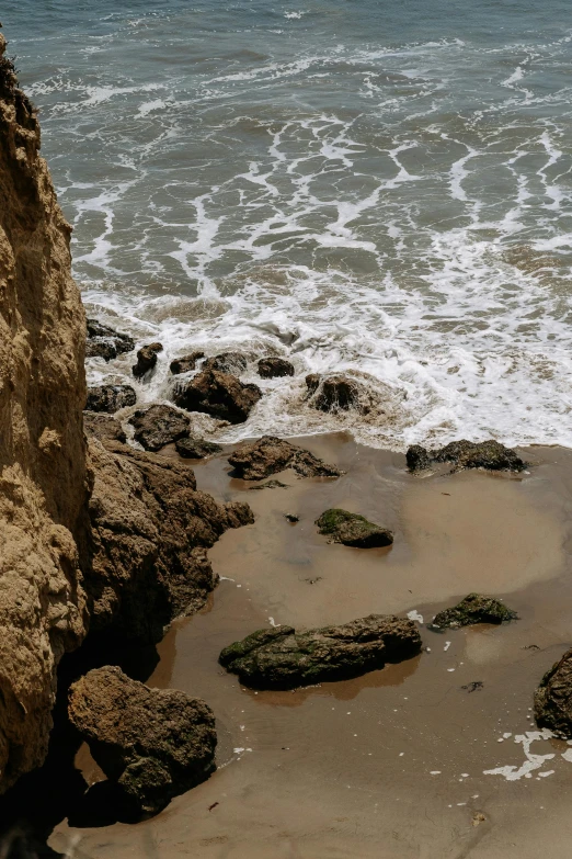 a man riding a surfboard on top of a sandy beach, an album cover, unsplash, renaissance, chiseled formations, malibu canyon, ((rocks)), rivulets