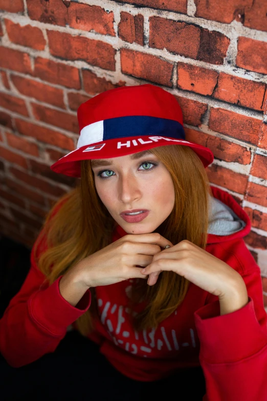 a woman in a red hat leaning against a brick wall, mrbeast, in style of heikala, patriotic, official store photo