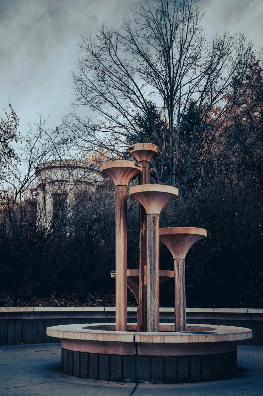 a fountain in a park with trees in the background, an abstract sculpture, unsplash contest winner, conceptual art, turrets, gloomy lighting, wooden supports, verner panton