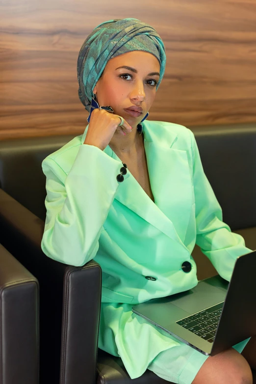 a woman sitting on a couch with a laptop, a colorized photo, inspired by Nil Gleyen, hurufiyya, teal suit, head scarf, office clothes, pastel green