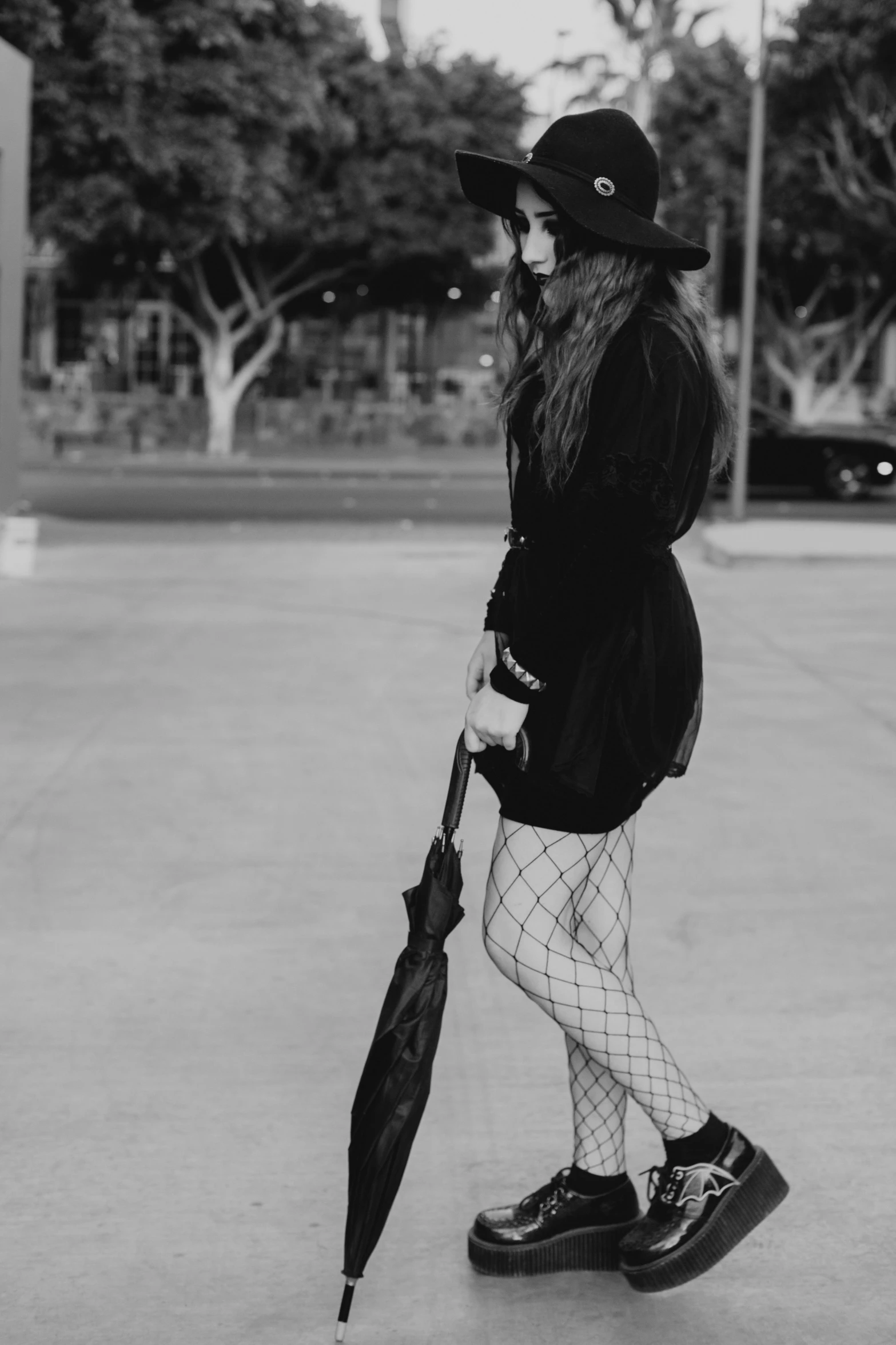 a black and white photo of a woman walking with an umbrella, a black and white photo, unsplash, fishnets pantyhose, witch clothes, concert, street fashion