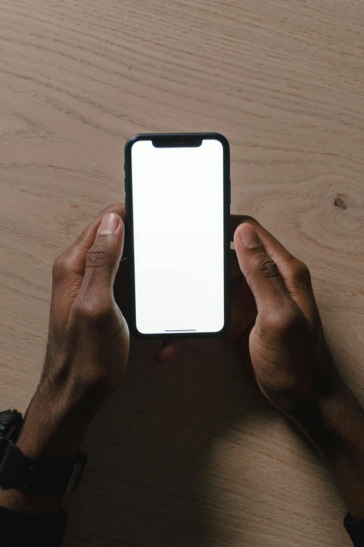 a person holding a cell phone with a white screen, by James Morris, trending on unsplash, ( ( dark skin ) ), sitting on a table, iphone wallpaper, no - text no - logo