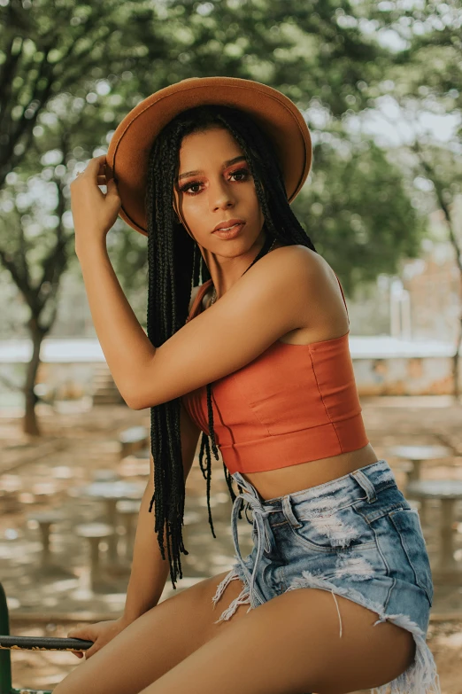 a woman sitting on a picnic table wearing a hat, by Briana Mora, trending on pexels, renaissance, dreadlock black hair, croptop and shorts, model standing pose, vests and corsets