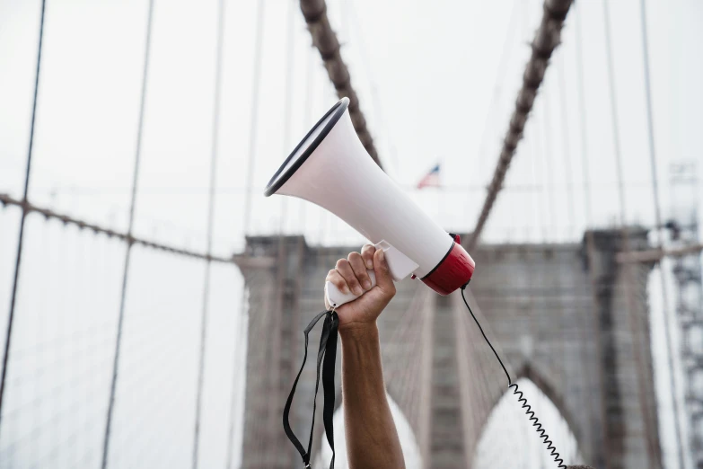 a man holding a megaphone in front of a bridge, trending on pexels, brooklyn, holding court, usa-sep 20, holding a staff