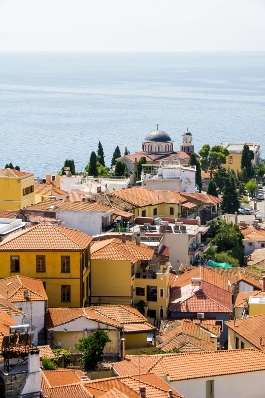 a group of buildings sitting on top of a hill next to the ocean, inspired by Edi Rama, renaissance, tiled roofs, greek nose, orange roof, photograph from above