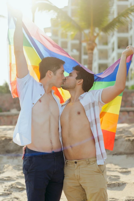 a couple of men standing next to each other on a beach, by Julia Pishtar, shutterstock, lgbt flag, making out, 🚿🗝📝