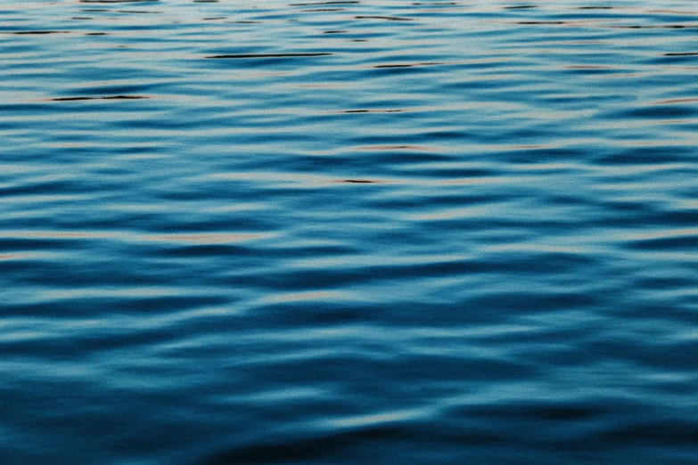 a boat floating on top of a body of water, a close up shot, dark blue water, heat ripples, subtle blue