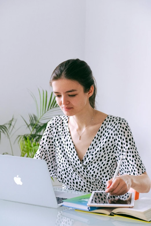 a woman sitting at a table working on a laptop, pexels contest winner, white with black spots, wearing a designer top, alina ivanchenko, with apple