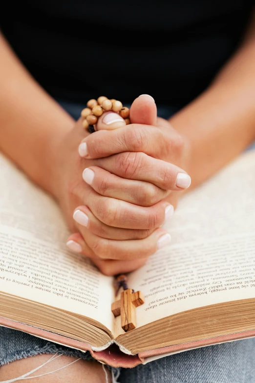 a woman holding a rosary sitting on top of an open book, hands pressed together in bow, stockphoto, multiple stories, large)}]