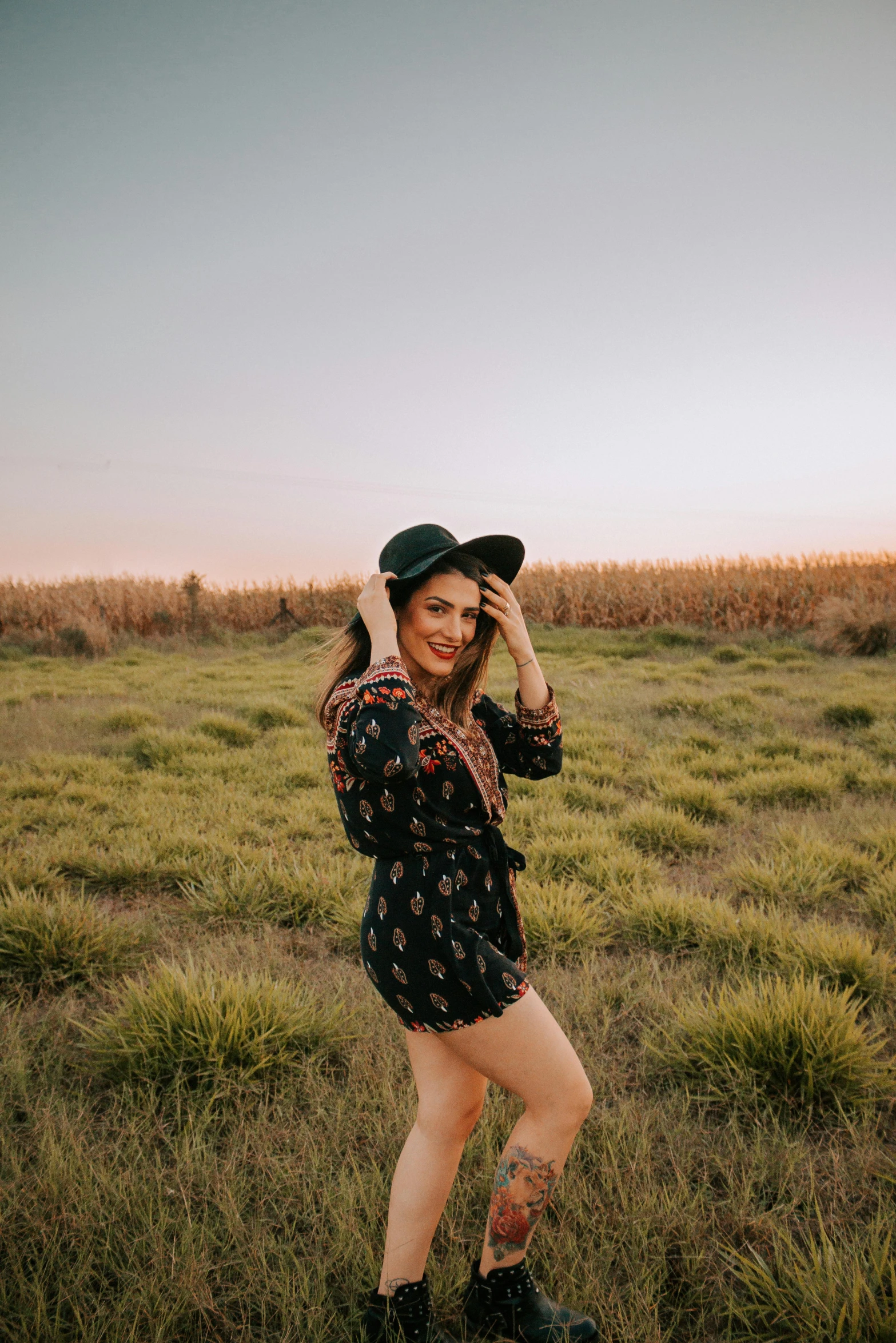 a woman standing in a field with a hat on, trending on pexels, dressed in a top and shorts, fun pose, late evening, lachlan bailey