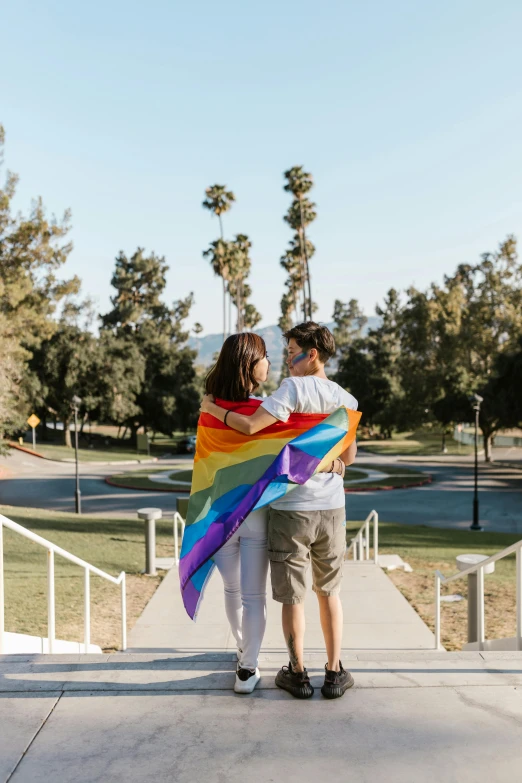 a man and a woman holding a rainbow colored kite, trending on unsplash, walking at the park, the city of santa barbara, holding a white flag, walkway