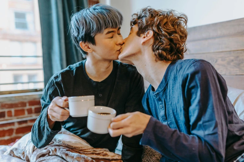 a couple of people sitting on top of a bed, trending on pexels, is ((drinking a cup of tea)), lesbian kiss, south korean male, cute boys