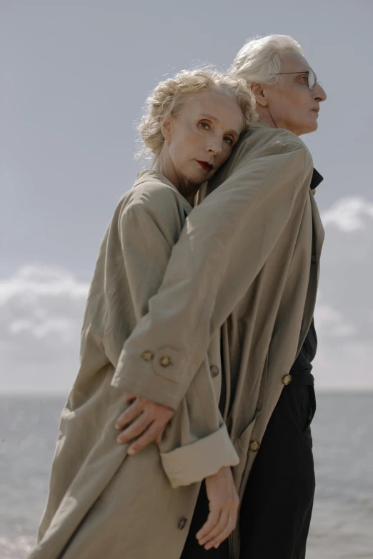 a man and a woman standing next to each other on a beach, poster art, by Lee Gatch, unsplash, renaissance, trench coat, albino skin, embracing, elongated arms