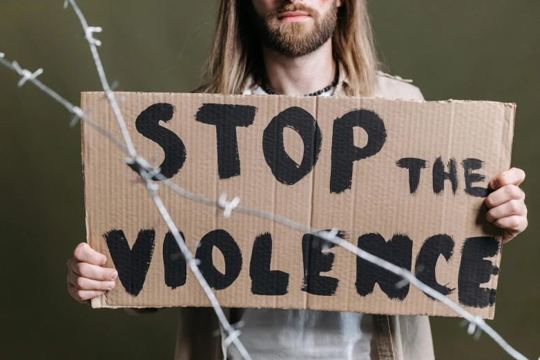 a man holding a sign that says stop the violence, trending on pexels, avatar image, background image, ripped fabric, made of cardboard