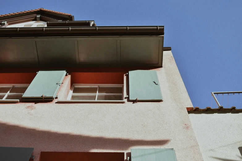 a building with shutters open on a sunny day, inspired by Wes Anderson, pexels contest winner, view from ground, muted coloures, passive house, payne's grey and venetian red