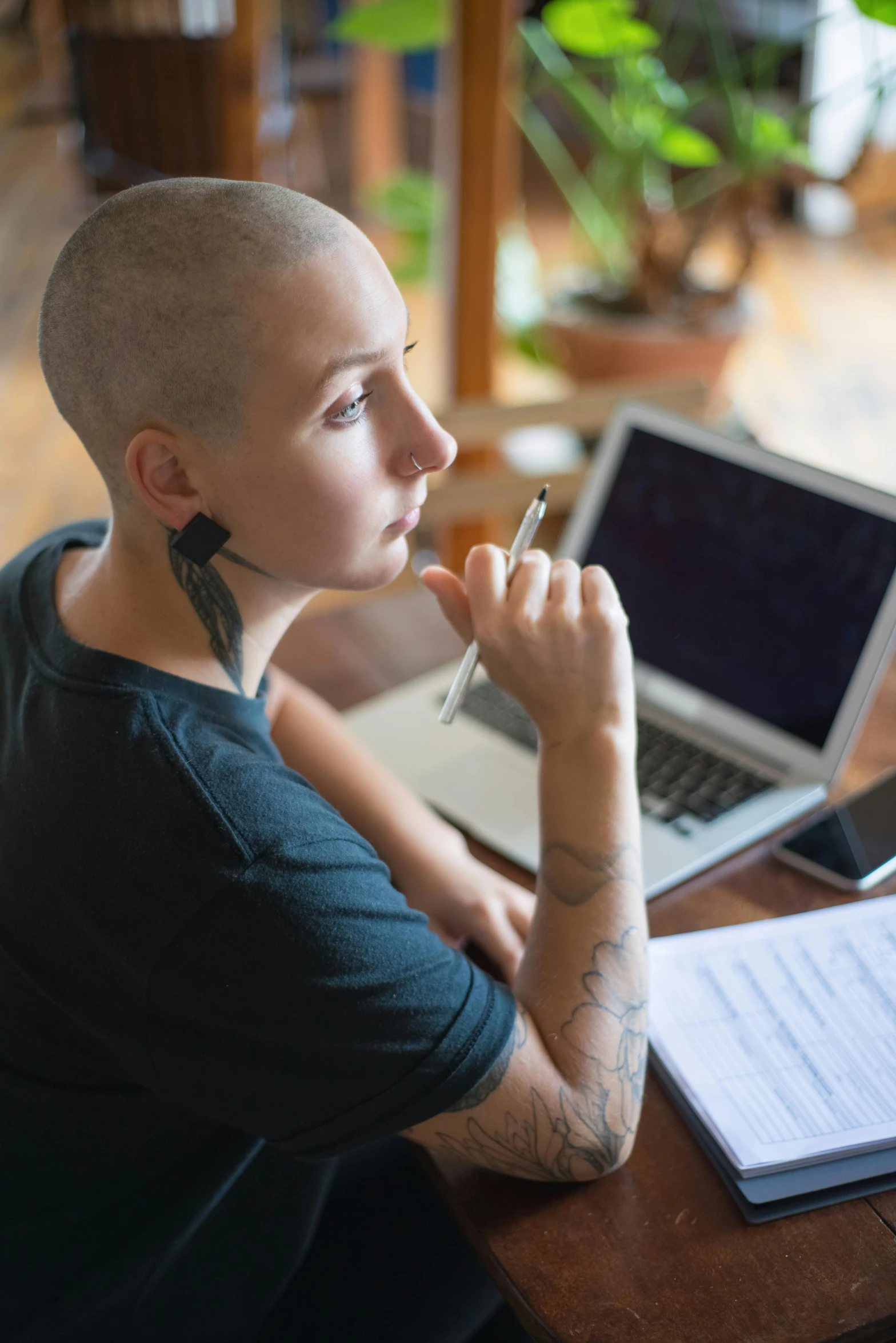 a man sitting at a table in front of a laptop computer, by artist, pexels, buzz cut hair, photo of young woman, tattooed, pondering