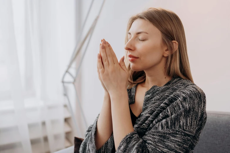 a woman sitting on a couch with her eyes closed, trending on pexels, hurufiyya, praying posture, profile image, wearing cross on robe, acupuncture treatment