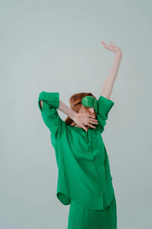 a woman wearing a green shirt and green pants, by Rebecca Horn, trending on pexels, visual art, waving robe movement, red haired young woman, showstudio, blindfold