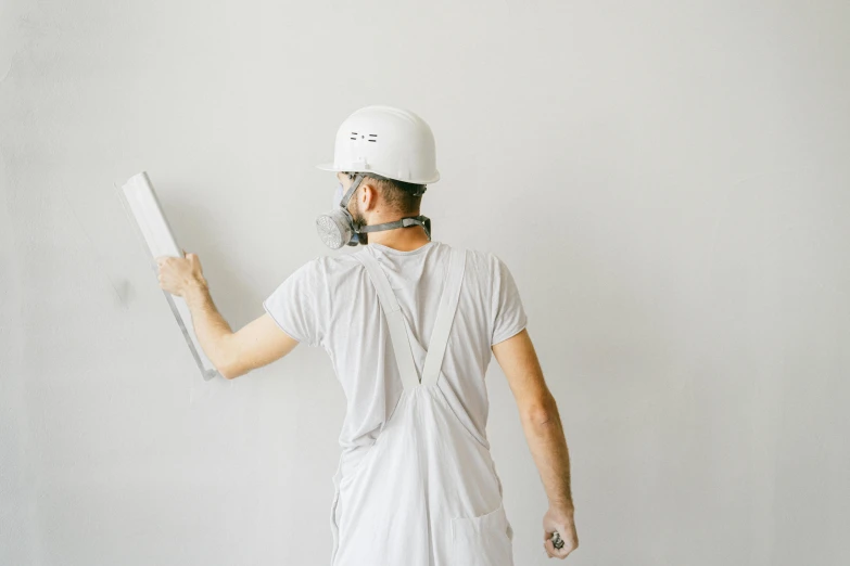 a man in a helmet is painting a wall, a minimalist painting, by Andries Stock, pexels contest winner, arbeitsrat für kunst, white backround, grey, commercial, white