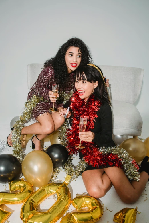 a couple of women sitting on top of a bed, pexels, kitsch movement, new years eve, gold and red accents, latinas, vine