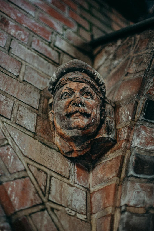 a statue of a man on a brick wall, inspired by Sir Jacob Epstein, unsplash, renaissance, ceramic looking face, chimney, gothic face, square face