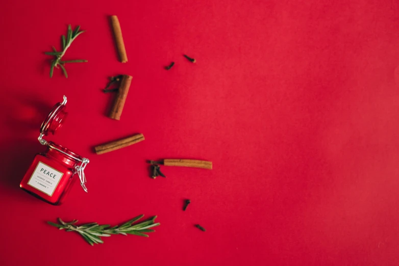 a jar of cinnamon and rosemary on a red background, an album cover, trending on pexels, minimalism, background image, red hot soldering iron, christmas, scattered props