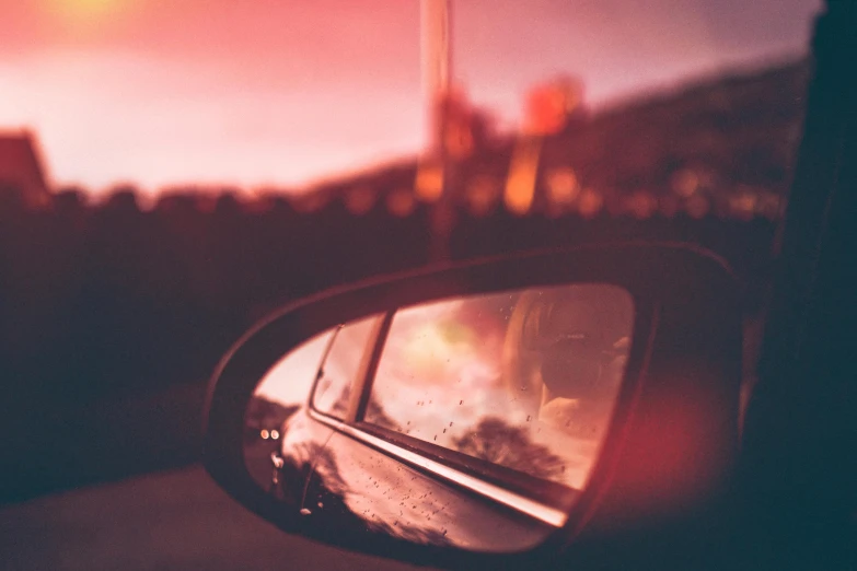 a rear view mirror of a car with a sunset in the background, inspired by Elsa Bleda, pexels contest winner, red tint, album cover, slight bokeh, pink reflections