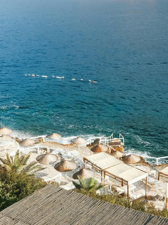 a beach filled with lots of umbrellas next to the ocean, greek pool, terraces, thumbnail, gold and white robes