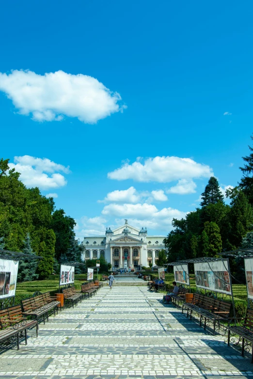 a walkway lined with benches in front of a building, by Antoni Brodowski, neoclassicism, monumental giant palace, profile image, blue skies, ( ( theatrical ) )