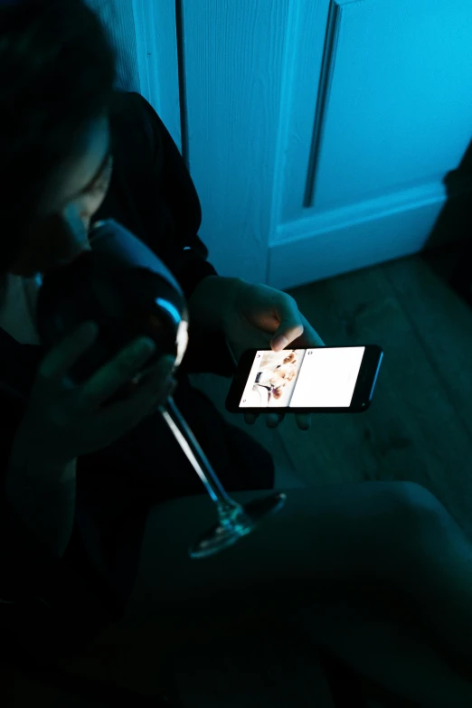 a woman sitting on the floor holding a glass of wine, a picture, inspired by Nan Goldin, pexels, happening, she is holding a smartphone, reading for a party, close up to the screen, 6 : 3 0 am