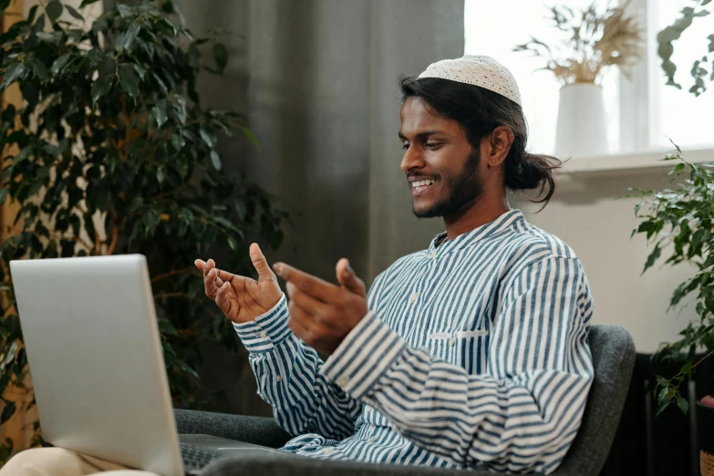 a man sitting in a chair in front of a laptop, inspired by Ismail Gulgee, pexels contest winner, hurufiyya, wearing a kurta, gestures, bringing people together, ( ( theatrical ) )