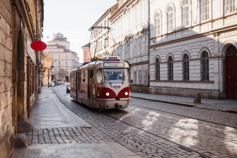 a red and white train traveling down a street next to tall buildings, unsplash contest winner, viennese actionism, lviv historic centre, profile image, square, trams